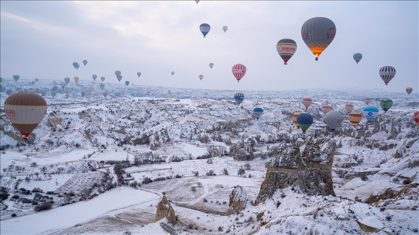 Balonat me ajër të nxehtë fluturojnë mbi oxhaqet e zanave të mbuluara me borë në Kapadokya